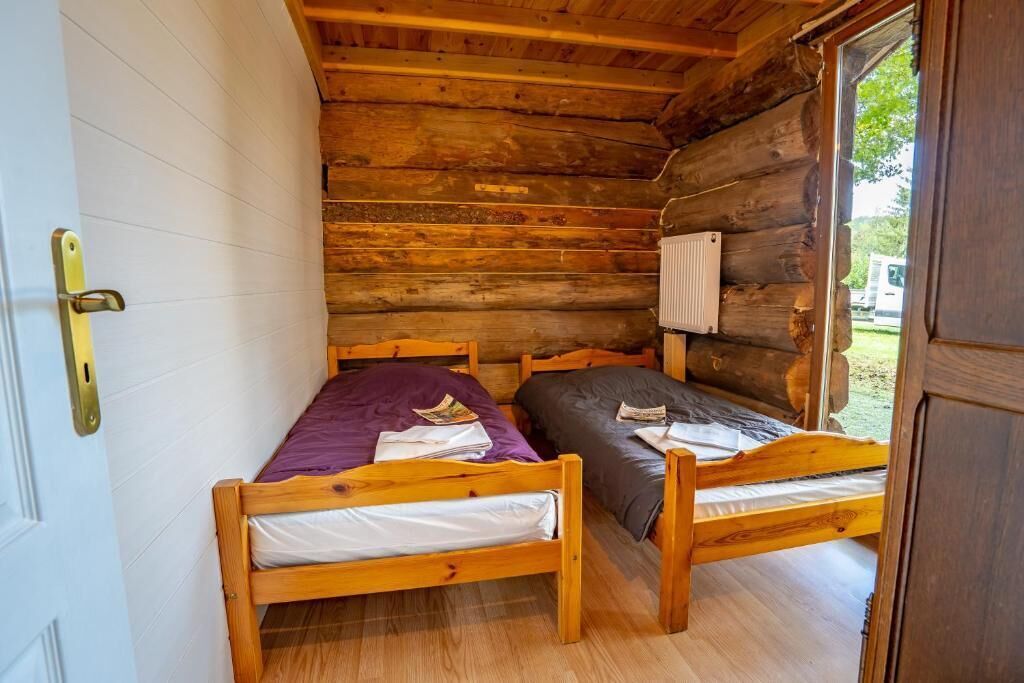 A log cabin room with two wooden beds, a white door, and a window.