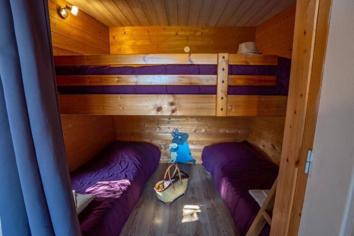 Eine kleine Holzhütte mit zwei Etagenbetten, einer Holzbalkendecke und einem kleinen Tisch mit einem Korb.