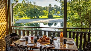 A wooden deck with a table set for breakfast, overlooking a lake and greenery.