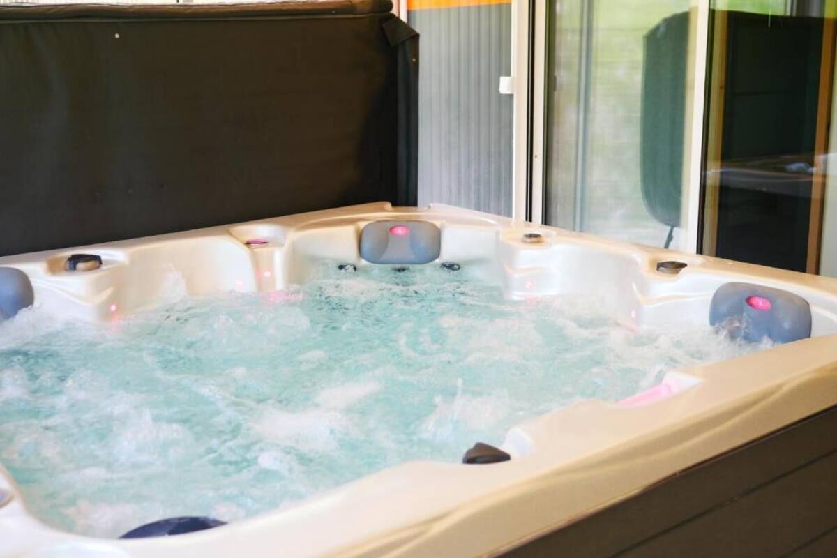 Ein Whirlpool mit sichtbaren Düsen, einer Abdeckung und einer Glasabtrennung.
