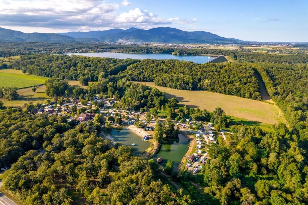 An aerial view of a town with a lake, surrounded by dense forests, and a small cluster of buildings.