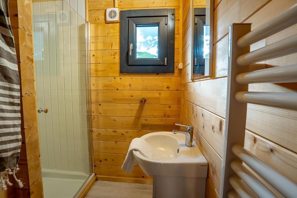 A wooden cabin bathroom with a shower, a sink, and a window.
