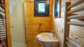 A wooden cabin bathroom with a shower, a sink, and a window.