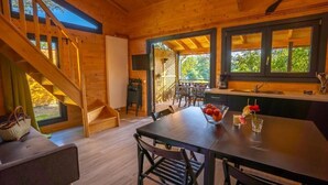 A wooden cabin interior with a dining table, chairs, a staircase, and a kitchen area.