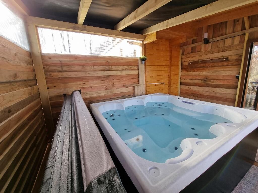 A wooden cabin with a hot tub, wooden walls, and a window.