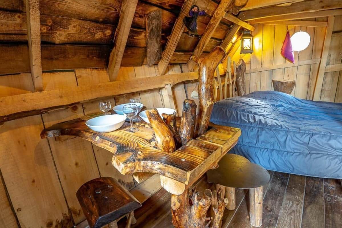 Ein rustikales Holzhaus-Interieur mit einem Bett, einem Tisch mit Schüssel und Weingläsern sowie einer Bank.