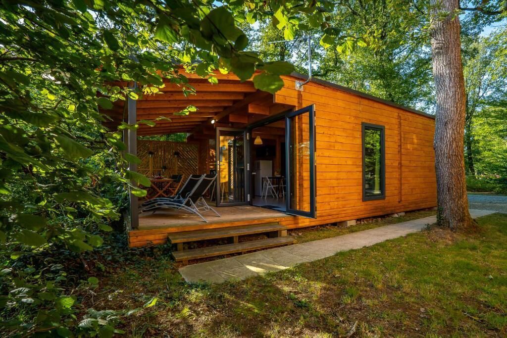 Una cabaña de madera con un porche cubierto, una puerta de cristal y un pequeño espacio de estar al aire libre.