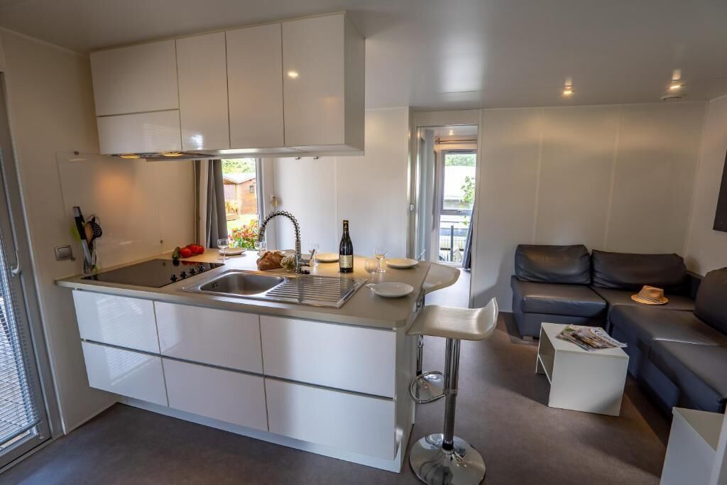 Une cuisine moderne avec des meubles blancs, un îlot central et un coin repas comprenant un canapé et une table basse.