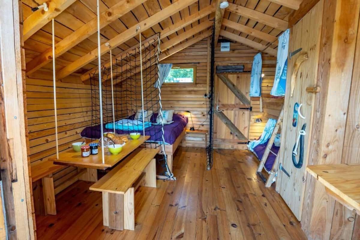 Eine Holzhütte mit Schlafkoje, einem Esstisch mit Speisen und einem kleinen Fenster.