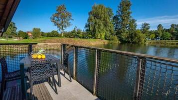 A deck with a table and chairs, overlooking a lake with a fence.