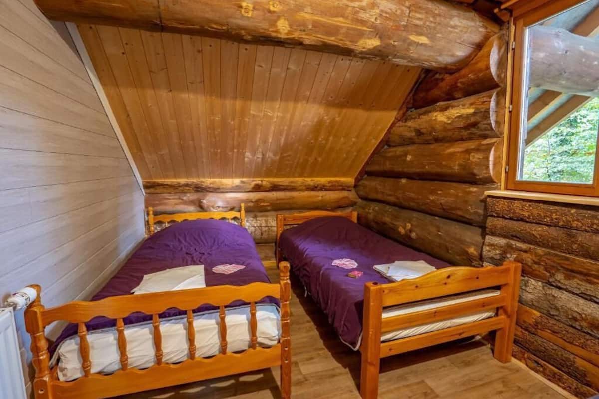 Ein Blockhauszimmer mit zwei Holzbetten, einem Fenster und einer Holzbalkendecke.