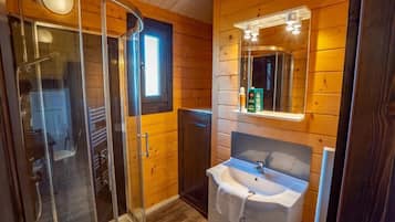 Interior de madera con cabina de ducha de vidrio, lavamanos con espejo y ventana.