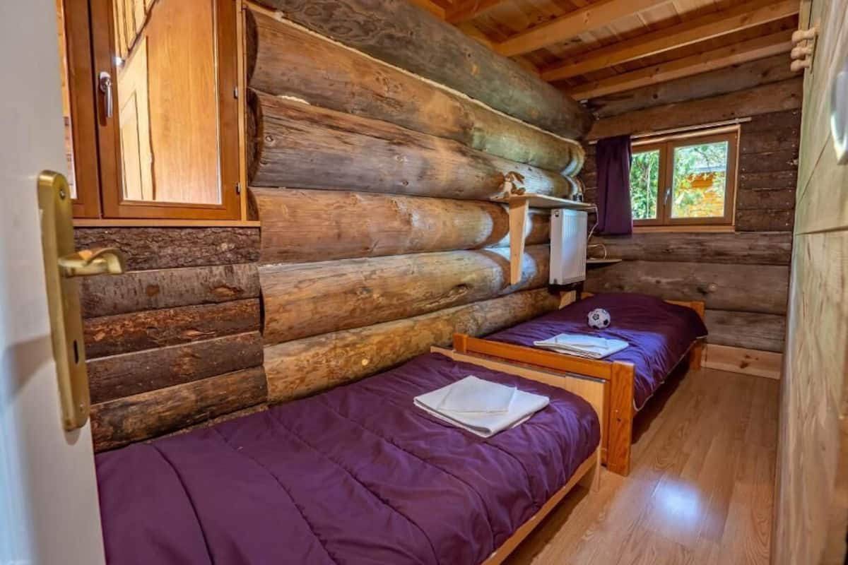 Ein Blockhauszimmer mit zwei Betten, einem Fenster mit Aussicht und einer Holztür.