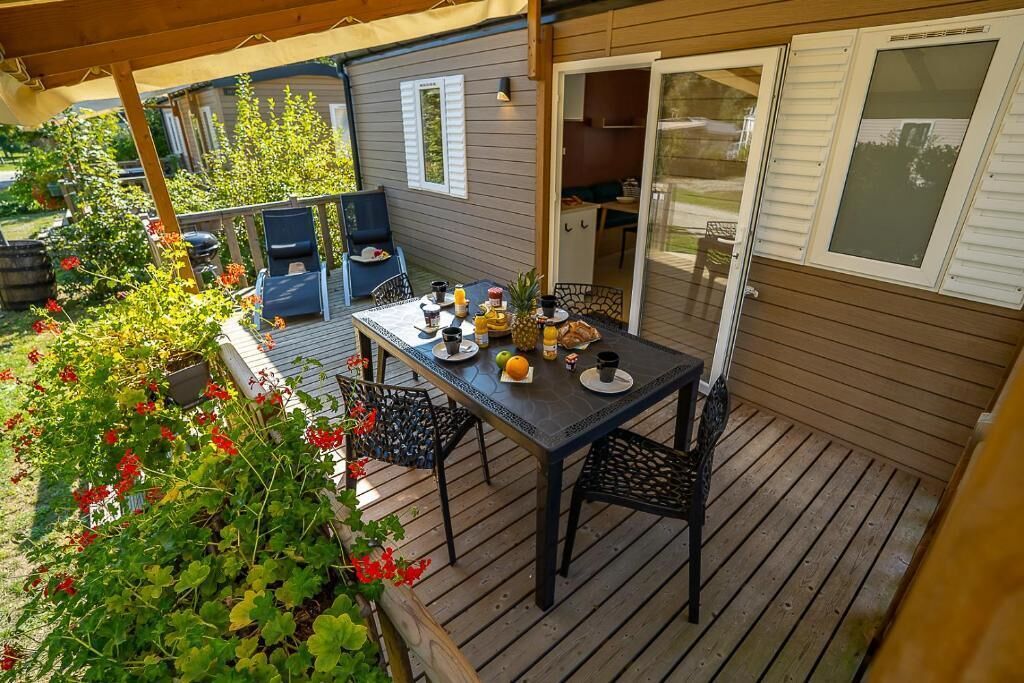 A covered patio with a table set for breakfast, outdoor seating, and a grill area.
