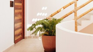 A hallway with a wooden door, a potted plant, and a staircase with a bamboo railing. - Casa Pola | Tropical Loft for 2 Near Beach & La Punta (Puerto Escondido)