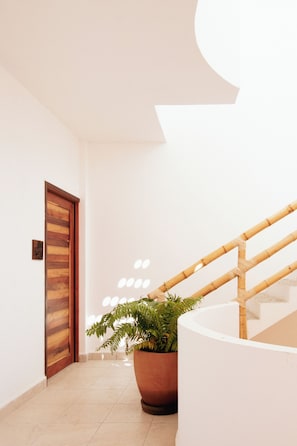A hallway with a wooden door, a potted plant, and a staircase with a bamboo railing. - Casa Pola | Tropical Loft for 2 Near Beach & La Punta (Puerto Escondido)