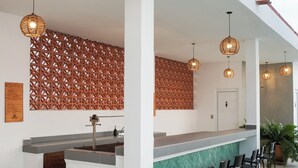 A reception area with a counter, chairs, wicker pendant lights, and a patterned wall. - Casa Pola | Tropical Loft for 2 Near Beach & La Punta (Puerto Escondido)
