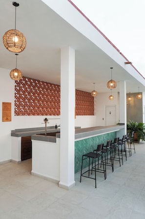A reception area with a counter, chairs, wicker pendant lights, and a patterned wall. - Casa Pola | Tropical Loft for 2 Near Beach & La Punta (Puerto Escondido)