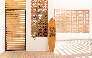 A wooden surfboard with text, a wooden slatted door, and a lattice wall with plants. - Casa Pola | Tropical Loft for 2 Near Beach & La Punta (Puerto Escondido)