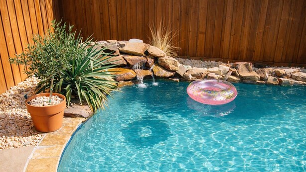 A swimming pool with clear water, a potted plant, and a rock waterfall. - Lil Pink Pool House • Coastal Cowgirl Charm • Walk to Historic Downtown McKinney (McKinney)