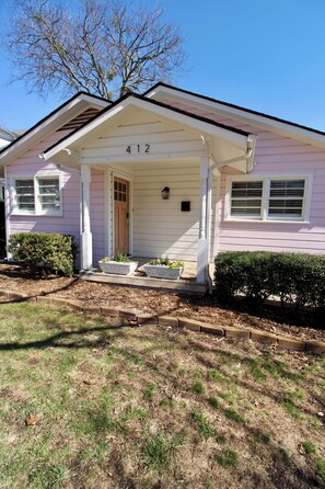 Ein pinkfarbenes Haus mit der Nummer 412, einer Veranda und einem kleinen Garten.