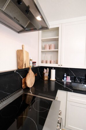 Eine moderne Küche mit schwarzem Arbeitsplatz, einer Edelstahl-Dunstabzugshaube, Holzschneidebrettern und einem weißen Schrank mit rosa Geschirr.