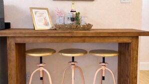 A wooden bar table with three stools, a framed sign on the wall, and a small decorative arrangement on the table. - Lil Pink Pool House • Coastal Cowgirl Charm • Walk to Historic Downtown McKinney (McKinney)