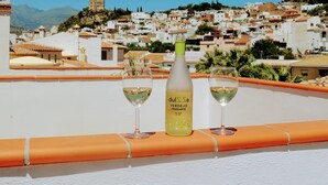 Terrassa amb una ampolla de vi i dues copes, amb vista a una vila de cases blanques i un turó al fons.