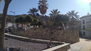 Un mur de pedra amb un passeig pavimentat, palmeres i un cel blau i clar.
