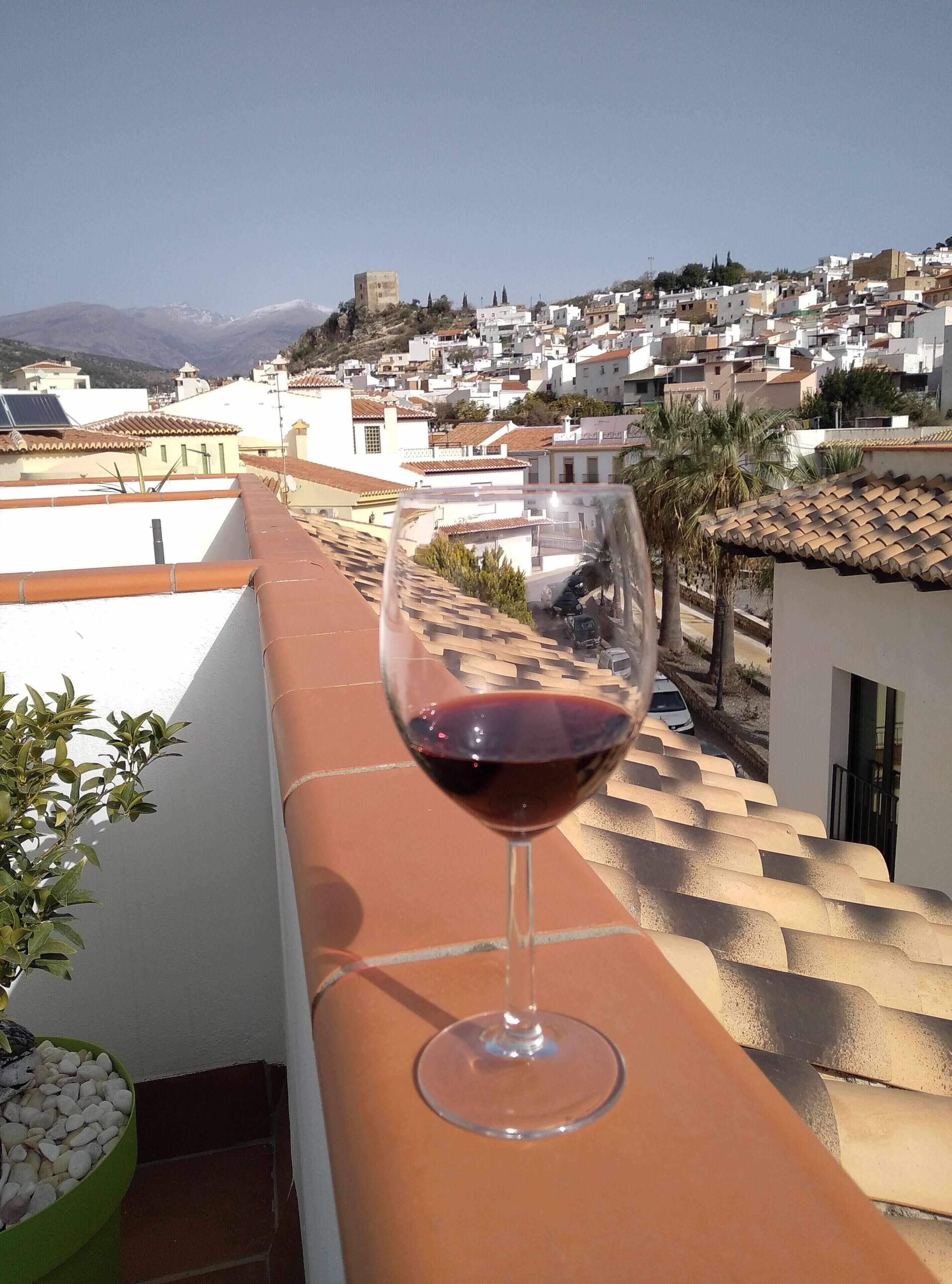 Un bicchiere di vino rosso su un balcone con vista su una cittadina dalle case bianche e una montagna sullo sfondo.