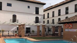 Una piscina amb aigua cristal·lina i blava, envoltada d'un edifici blanc amb moltes finestres i teulada de rajola.
