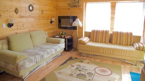 A cozy wooden cabin interior with a sofa, a couch, a TV, and a window with curtains. - Pocono Comfortable 2Bedroom Stay (Gouldsboro)