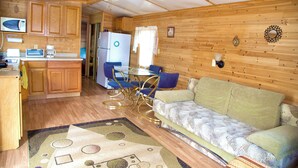 A compact kitchen with wooden cabinets, a microwave, a refrigerator, and a dining area with a table and chairs. - Pocono Comfortable 2Bedroom Stay (Gouldsboro)