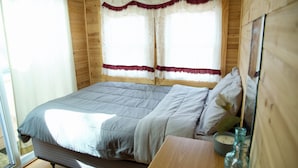 A wooden room with a bed, a window with curtains, and a bedside table with a clock and bottles. - Pocono Comfortable 2Bedroom Stay (Gouldsboro)
