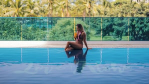A person sitting by a pool with a view of palm trees and a building in the background. - Premium Kalākaua Haus Kitchenette (Honolulu)