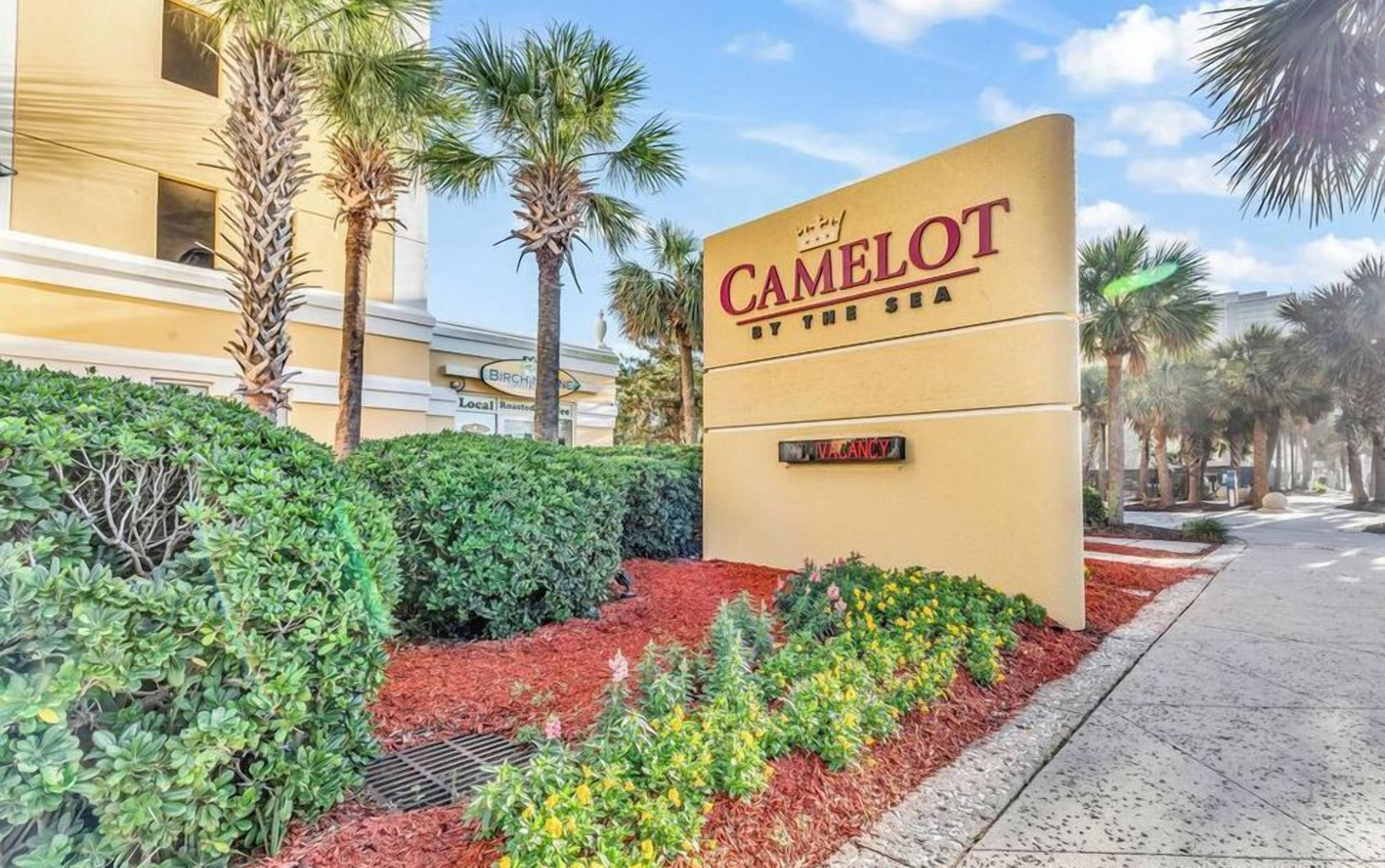 A hotel sign with 'CAMELOT BY THE SEA' and a 'VACANCY' sign.