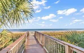 A wooden boardwalk leading to a beach with a clear sky and palm trees. - 1BR Oceanfront Paradise @Camelot! (Myrtle Beach)