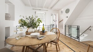 Un comedor con una mesa redonda, sillas, un florero con flores, botellas de vino y copas.