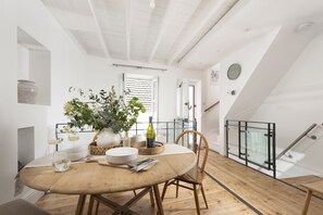 Un coin repas avec une table ronde, des chaises, un vase avec des fleurs, des bouteilles de vin et des verres.