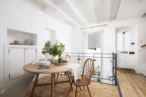 Un coin repas avec une table et des chaises en bois, un vase avec des plantes et une bouteille de vin.