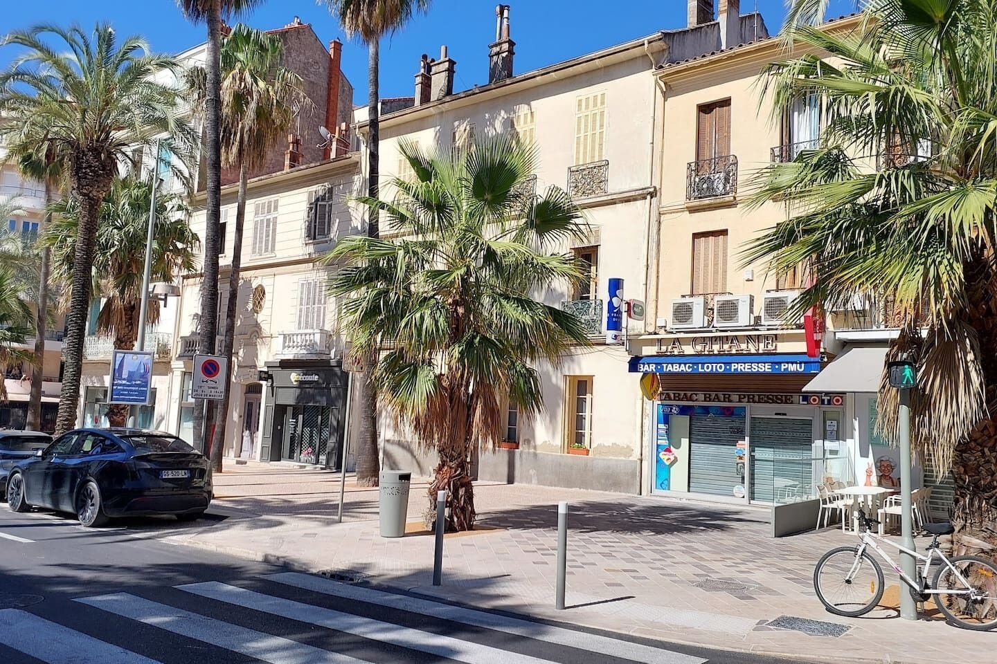 A street scene with a building that has a sign for a bar, tobacco, lottery, and PMU.