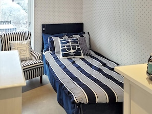 Una cama individual con ropa de cama a rayas, una silla con cojines a rayas y una pared con estampado.