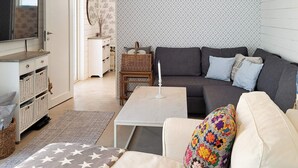 Un soggiorno con un divano, un tavolino da caffè, una TV, una poltrona in vimini e una parete decorata.