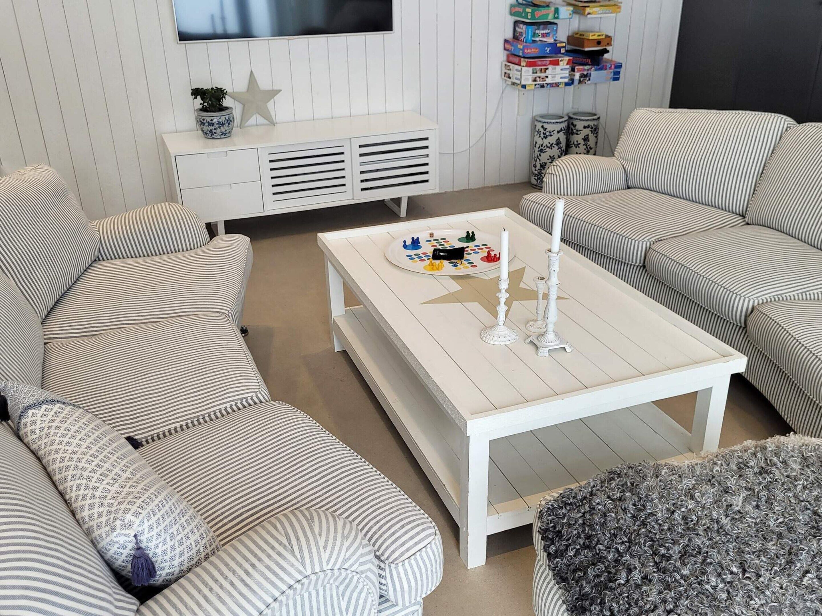 Un salon avec des canapés à rayures, une table basse blanche ornée de bougies et un téléviseur fixé au mur.
