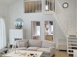 Una habitación amplia con un sofá a rayas, un armario blanco y una escalera que lleva a un nivel superior.