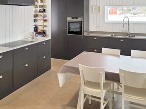 A modern kitchen with a built-in oven, a dining table with chairs, and a window with a view of the outside. - 5 Star Holiday Home in Ellos (Ellos)