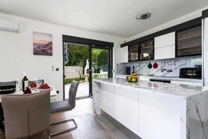 Una cocina moderna con encimera de mármol, un comedor con mesa y sillas, y vistas al exterior.