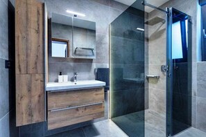 A modern bathroom with a wooden vanity, a glass shower enclosure, and a large mirror. - Holiday house LAVANDA with pool and panoramic seaview (Risika)