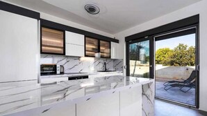 Een moderne keuken met marmeren aanrechtbladen, een inbouwoven en een schuifpui naar een balkon met een stoel.