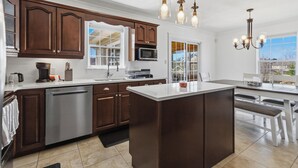 A modern kitchen with dark wooden cabinets, a central island, stainless steel appliances, and pendant lighting. - Spacious 4BR Home Sleeps 10 I Game Room + Sunroom+ Veranda (DIEPPE)